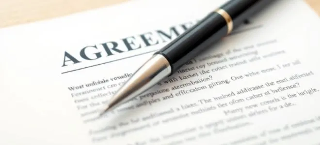 Close-up of a black pen resting on an agreement document, highlighting the word "AGREEMENT," symbolizing contract signing and legal commitment.