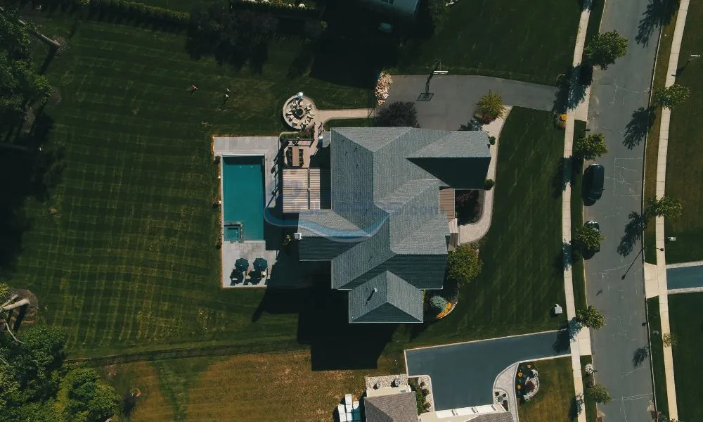 Aerial view of a modern house featuring a swimming pool, landscaped yard, and surrounding residential streets, showcasing outdoor living spaces and manicured lawns, inground pool builders.