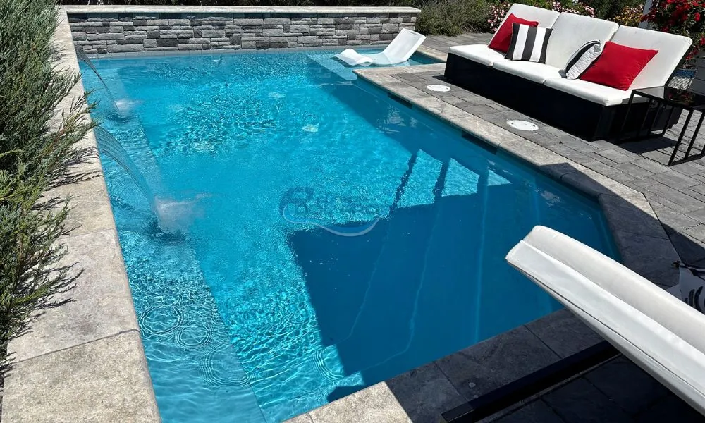 Luxury outdoor custom swimming pool with crystal-clear water, surrounded by modern lounge chairs and a stylish black sofa. The pool area features stone accents and a relaxing atmosphere, perfect for summer leisure and entertainment.