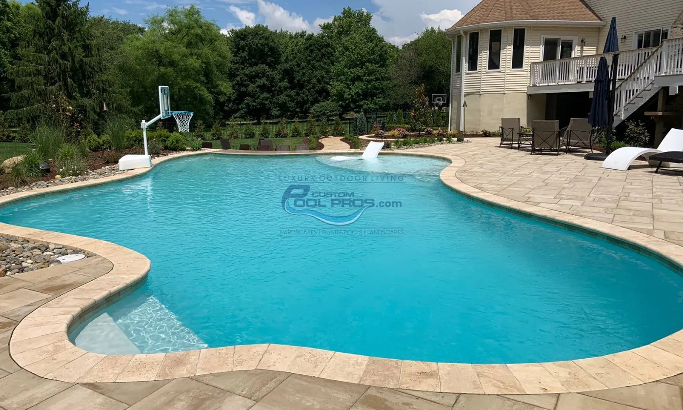 freeform gunite inground pool with bull nose coping, light blue turquoise water and sun tanning ledge with chaise lounge chair and basketball hoop